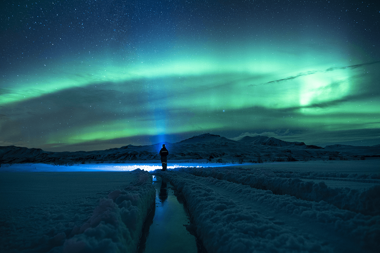 Viaggiatore osserva l'Aurora Boreale in un paesaggio innevato. I fenomeni naturali straordinari attraggono sempre più turisti in cerca di esperienze uniche.