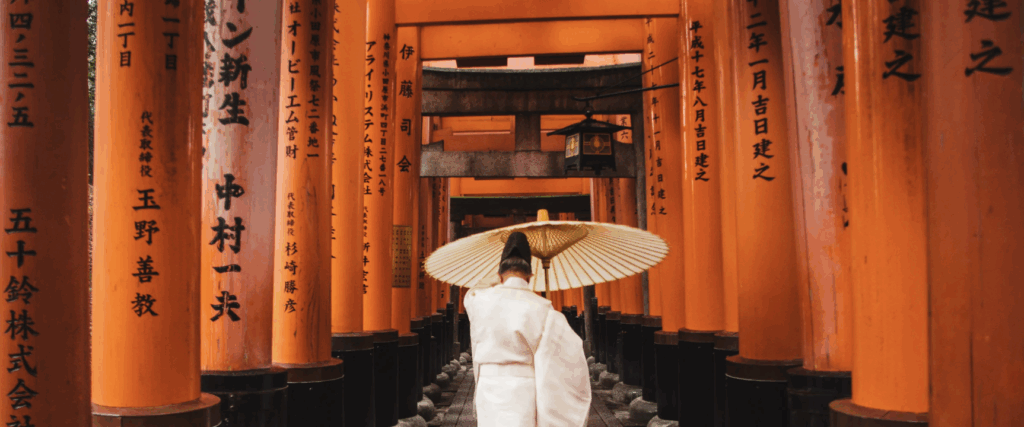 Tra i tunnel di torii rossi del celebre santuario Fushimi Inari, una viaggiatrice in kimono bianco avanza sotto l’ombrello tradizionale, immersa nella spiritualità di Kyoto.
