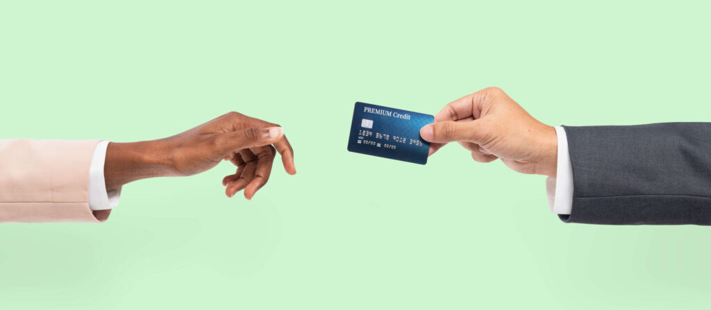 Mano di un uomo d'affari che porge una carta di credito a una donna, su sfondo verde pastello